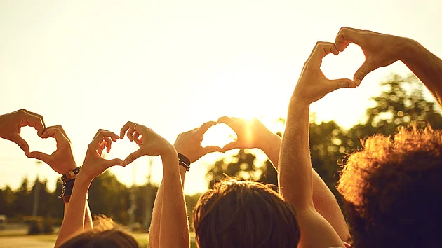 Hands of group friends in the shape of a heart against the sunset.